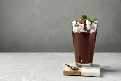 Glass of delicious hot chocolate with marshmallows and fresh mint on light grey marble table. Space for text