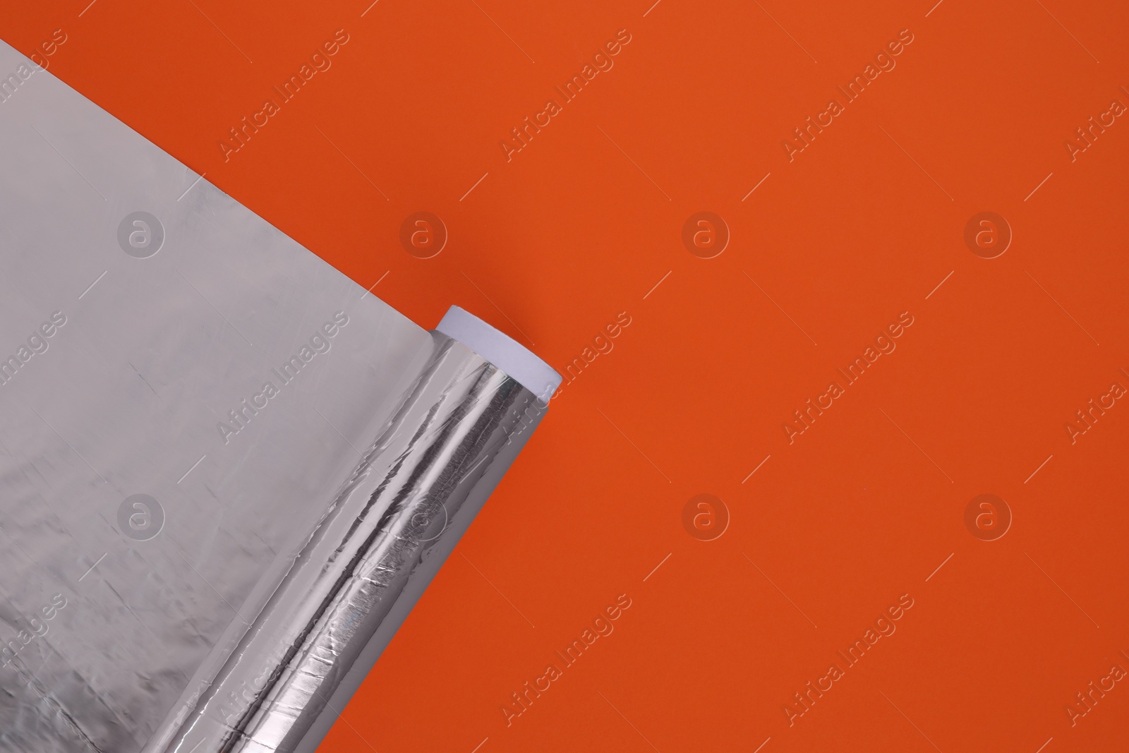 Photo of Roll of aluminum foil on orange background, top view. Space for text