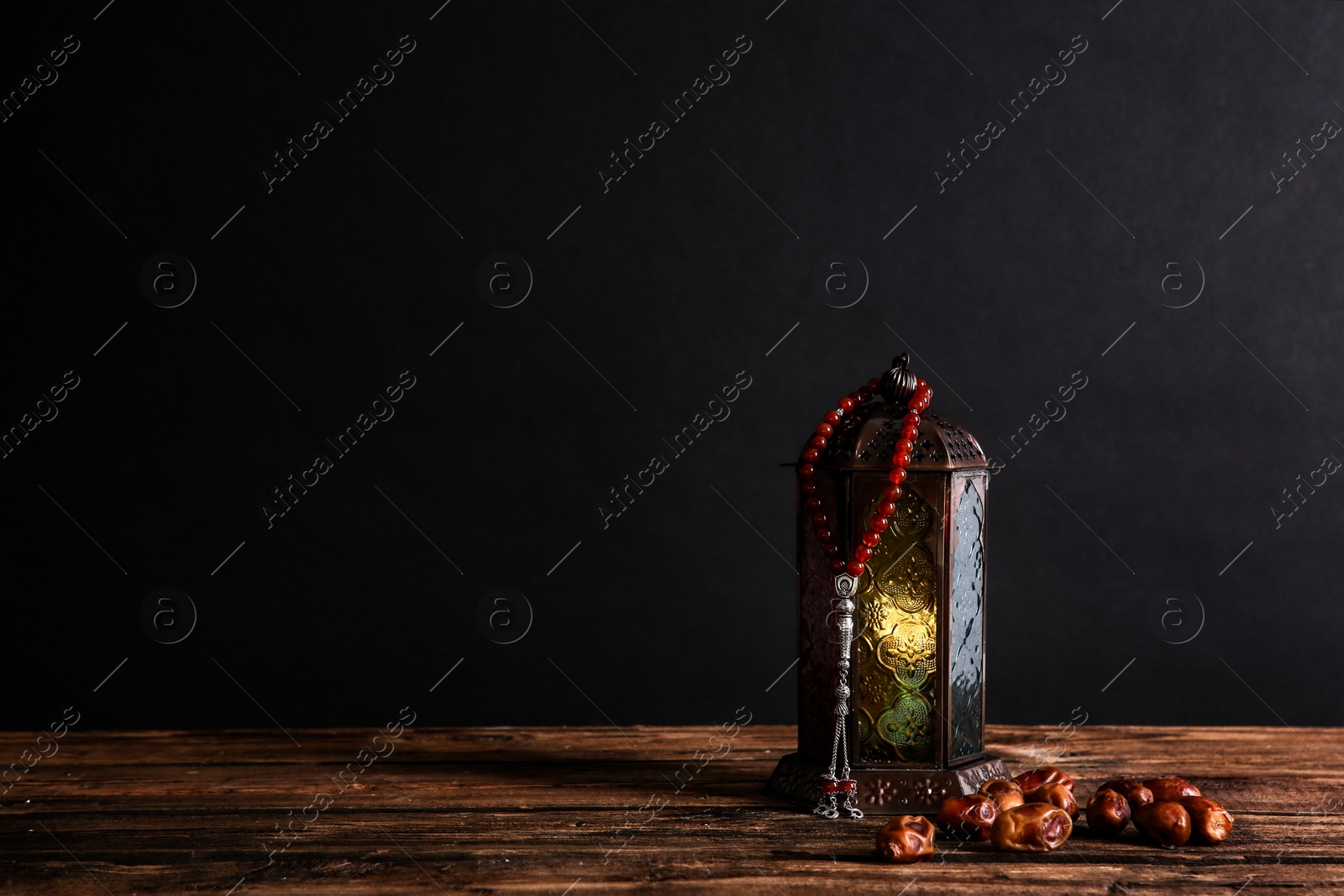 Photo of Muslim lamp, dates and prayer beads on wooden table against dark background. Space for text