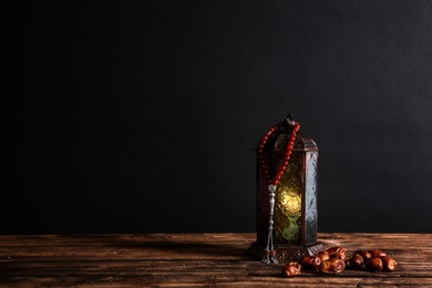 Muslim lamp, dates and prayer beads on wooden table against dark background. Space for text