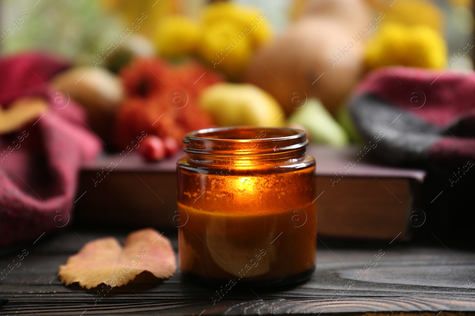 Photo of Burning scented candle and book on wooden table. Autumn season