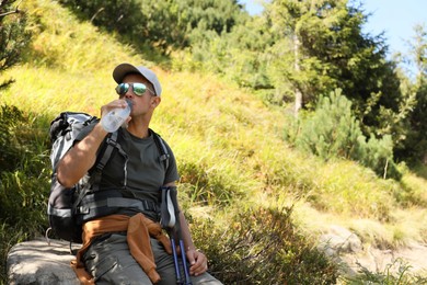 Photo of Tired hiker drinking water outdoors on sunny day