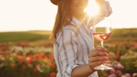 Woman with glass of wine in rose garden on sunny day, closeup