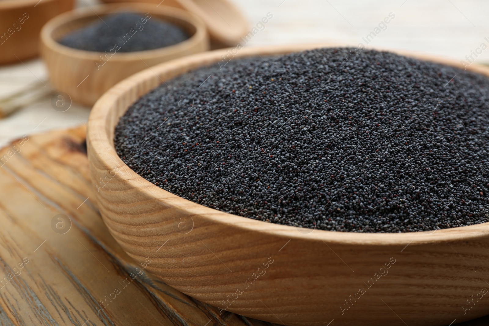 Photo of Poppy seeds in bowl on wooden board, closeup