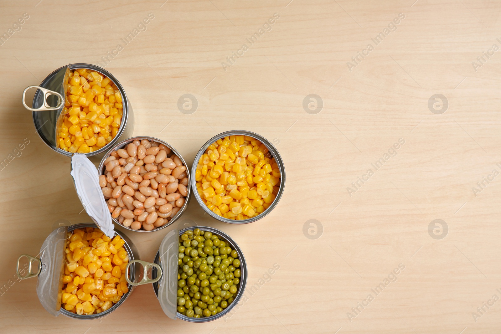 Photo of Open tin cans of conserved vegetables on wooden table, flat lay with space for text