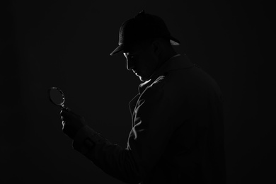 Photo of Old fashioned detective with magnifying glass on dark background, black and white effect