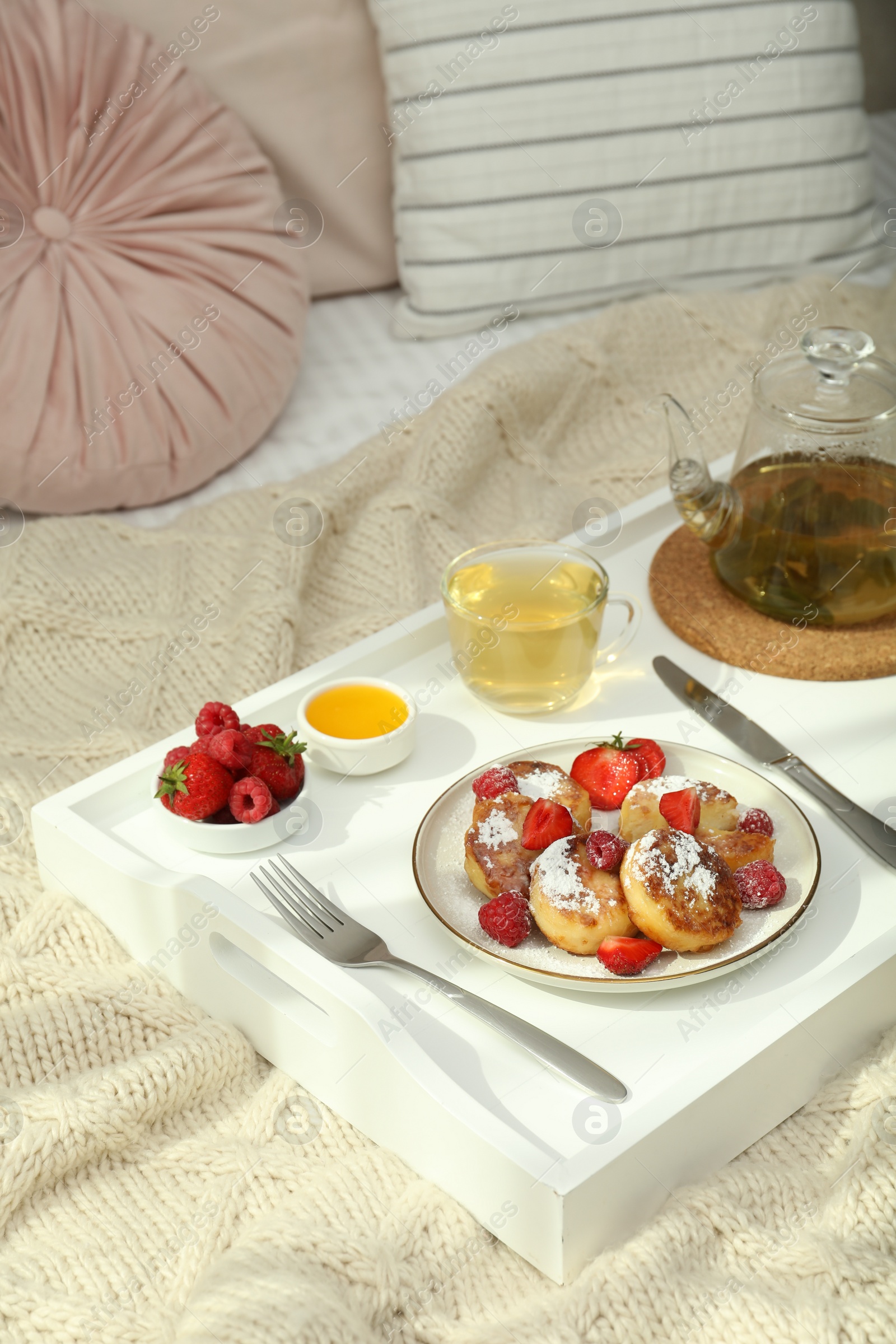 Photo of Tasty breakfast served in bedroom. Cottage cheese pancakes with fresh berries and icing sugar on wooden tray