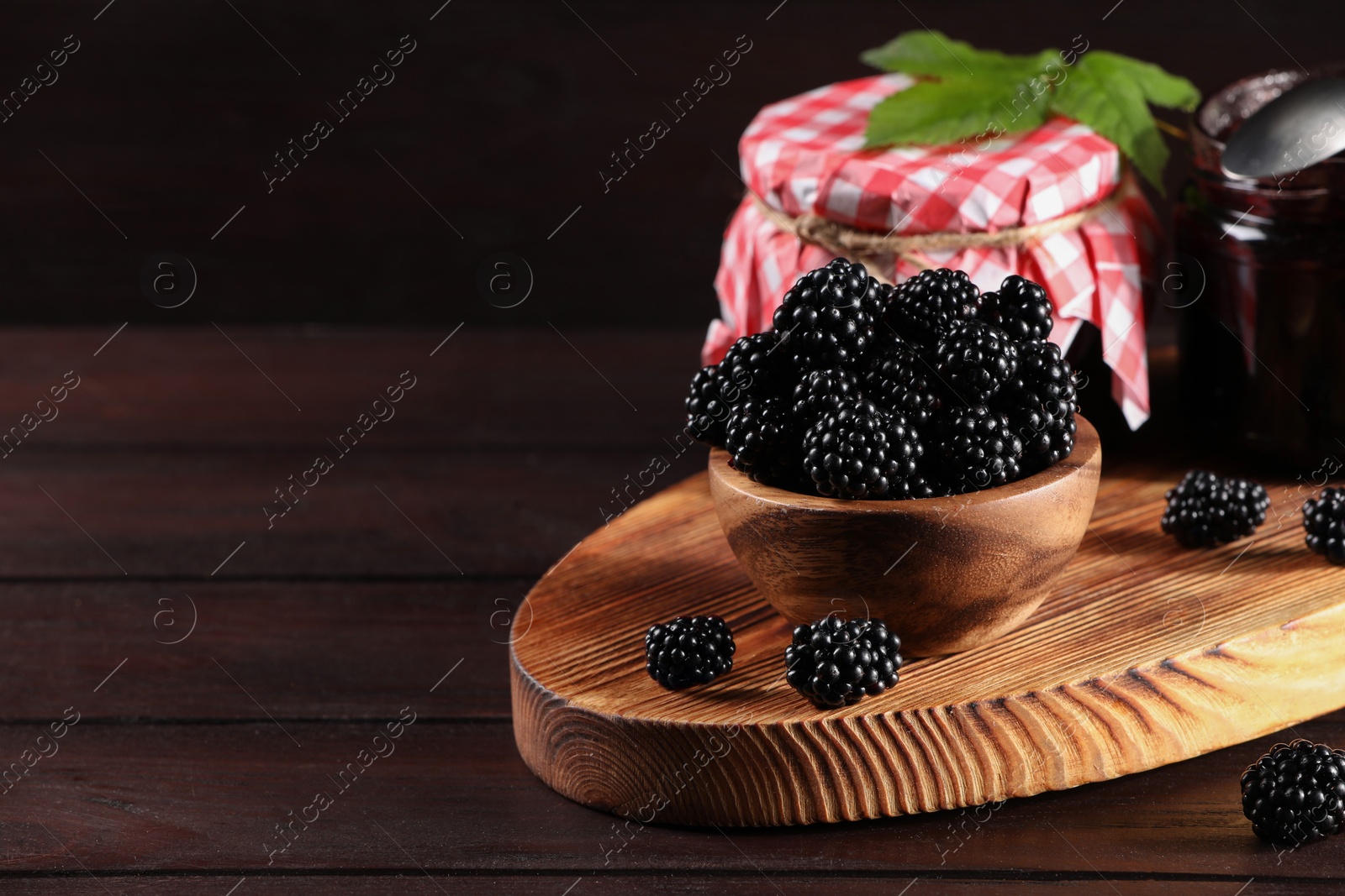 Photo of Fresh ripe blackberries, tasty jam and leaves on wooden table. Space for text