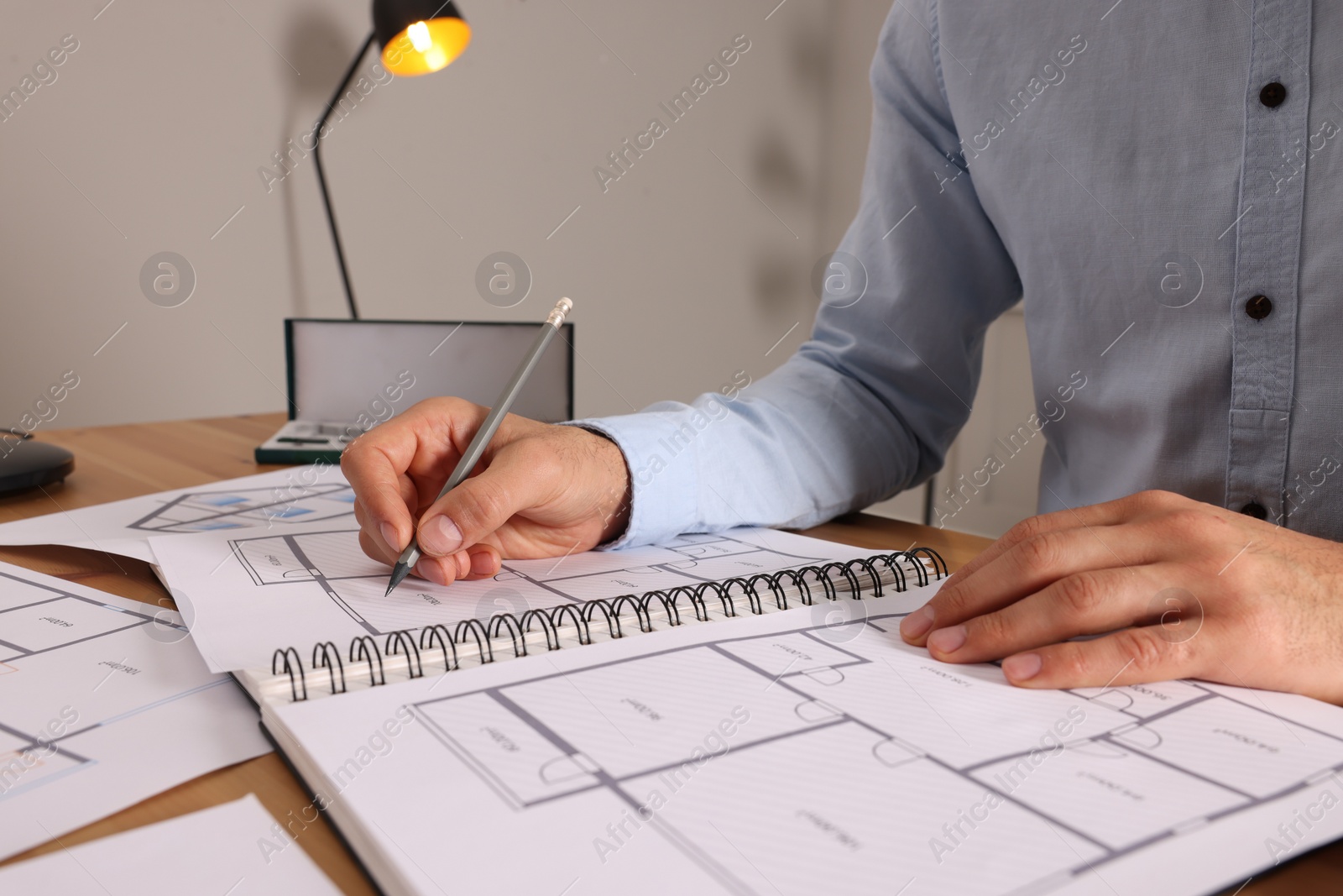 Photo of Man drawing in sketchbook with pencil at wooden table, closeup