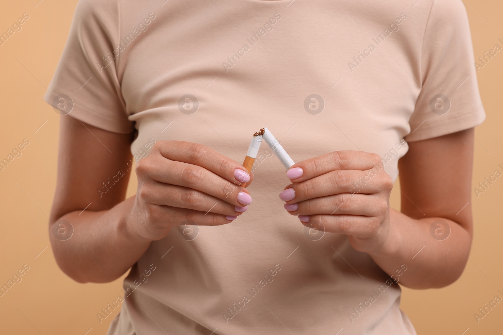 Photo of Stop smoking concept. Woman breaking cigarette on light brown background, closeup