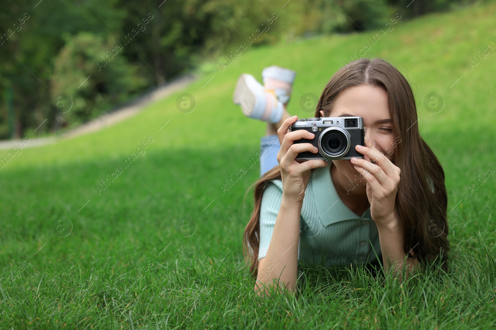 Photo of Young woman with camera taking photo on green grass outdoors, space for text. Interesting hobby