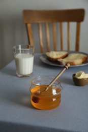 Jar with honey, milk and bread served for breakfast on grey table