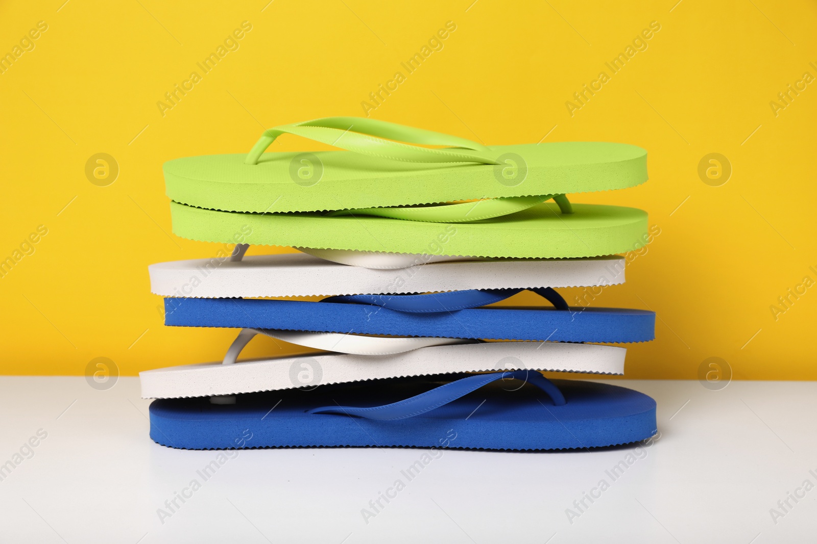 Photo of Stack of different flip flops on white table against yellow background