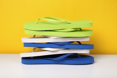 Photo of Stack of different flip flops on white table against yellow background