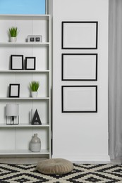 Photo of Stylish room interior with empty frames hanging on white wall near shelving unit