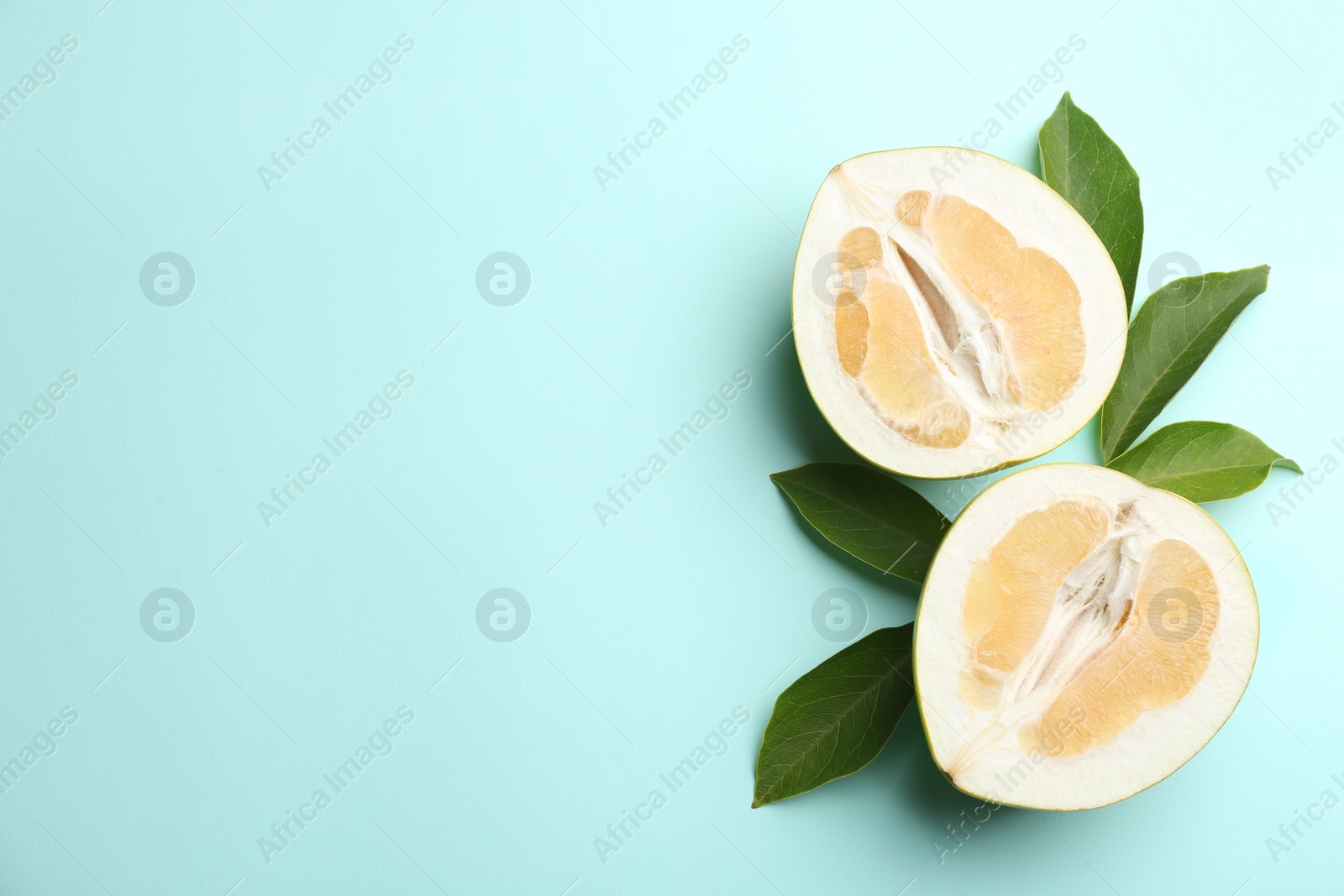 Photo of Fresh cut pomelo fruit with leaves on turquoise background, flat lay. Space for text