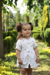 Cute little girl walking near green plants in park