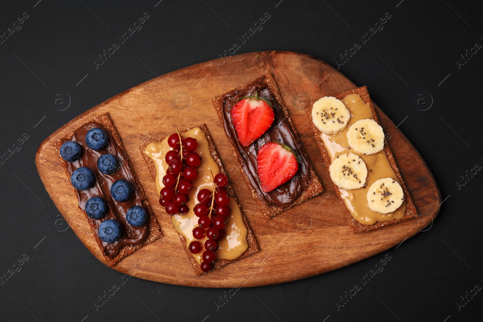 Photo of Fresh crunchy rye crispbreads with different toppings on black table, top view