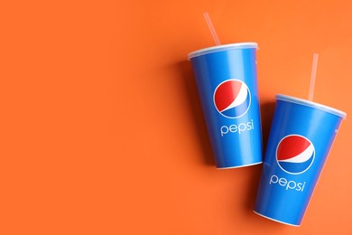 Photo of MYKOLAIV, UKRAINE - JUNE 9, 2021: Paper Pepsi cups on orange background, flat lay. Space for text
