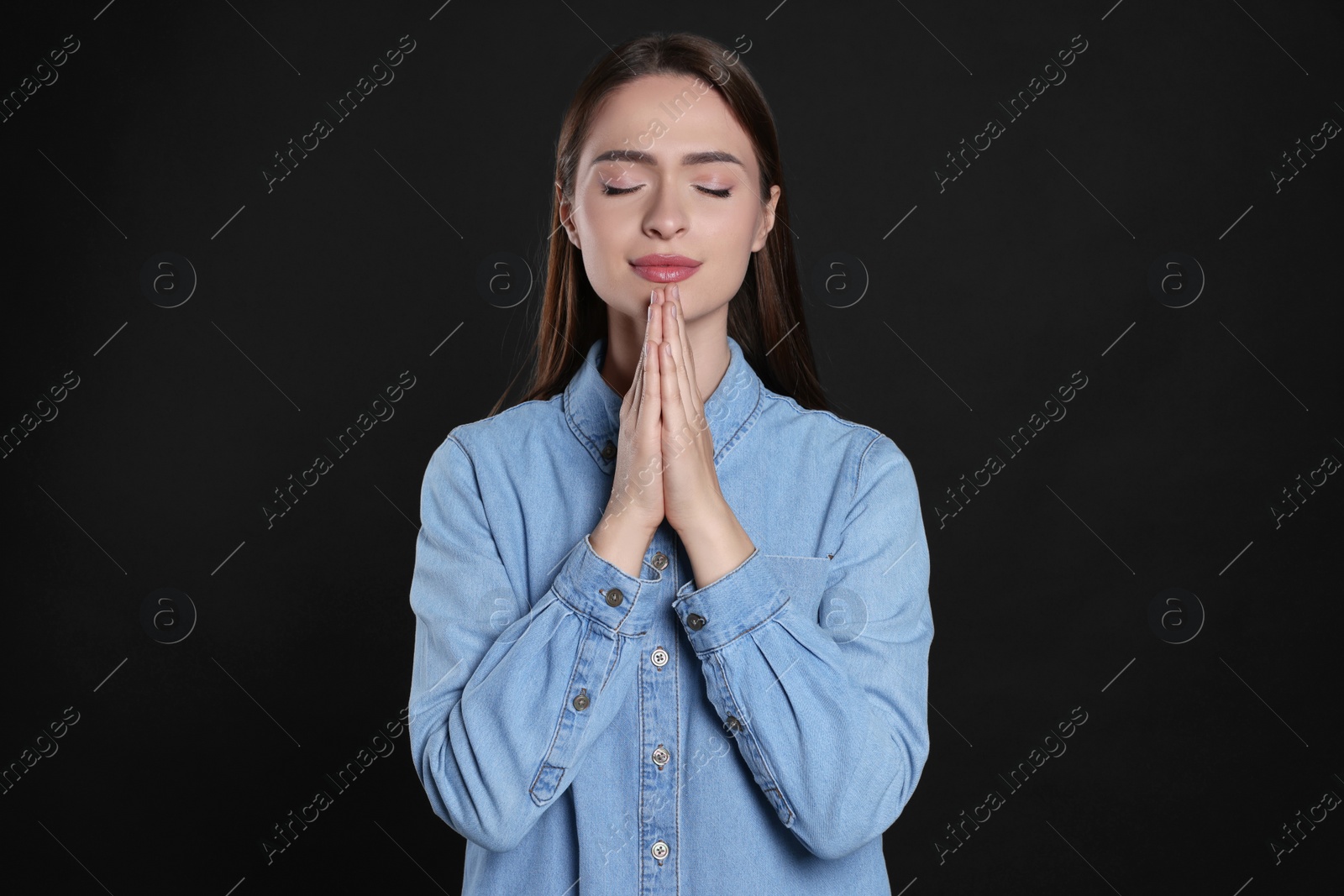 Photo of Woman with clasped hands praying on black background