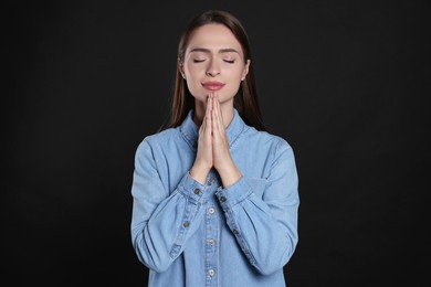 Woman with clasped hands praying on black background