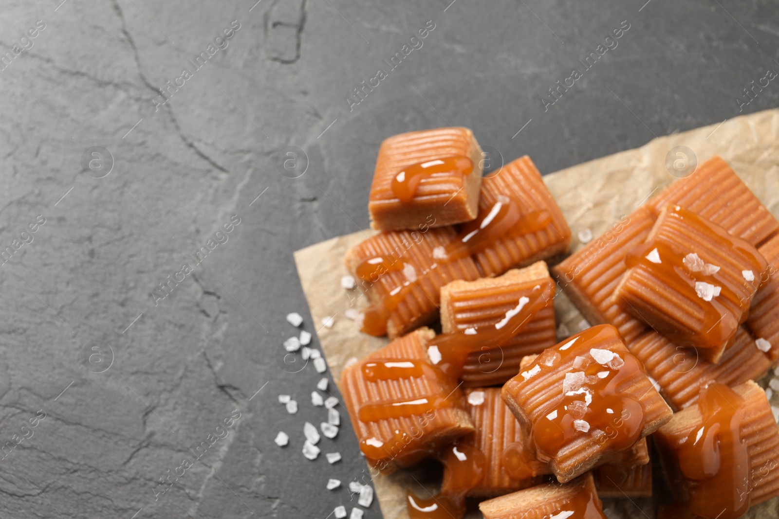 Photo of Tasty caramel candies with sauce and sea salt on grey table, above view. Space for text