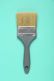 One paint brush with grey handle on turquoise background, top view