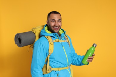 Photo of Happy tourist with backpack and thermo bottle on yellow background
