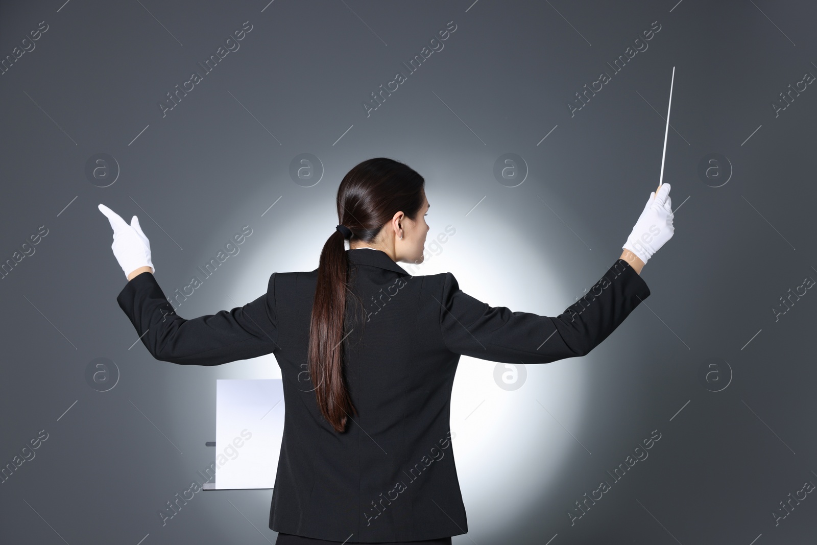 Photo of Professional conductor with baton and note stand on grey background, back view