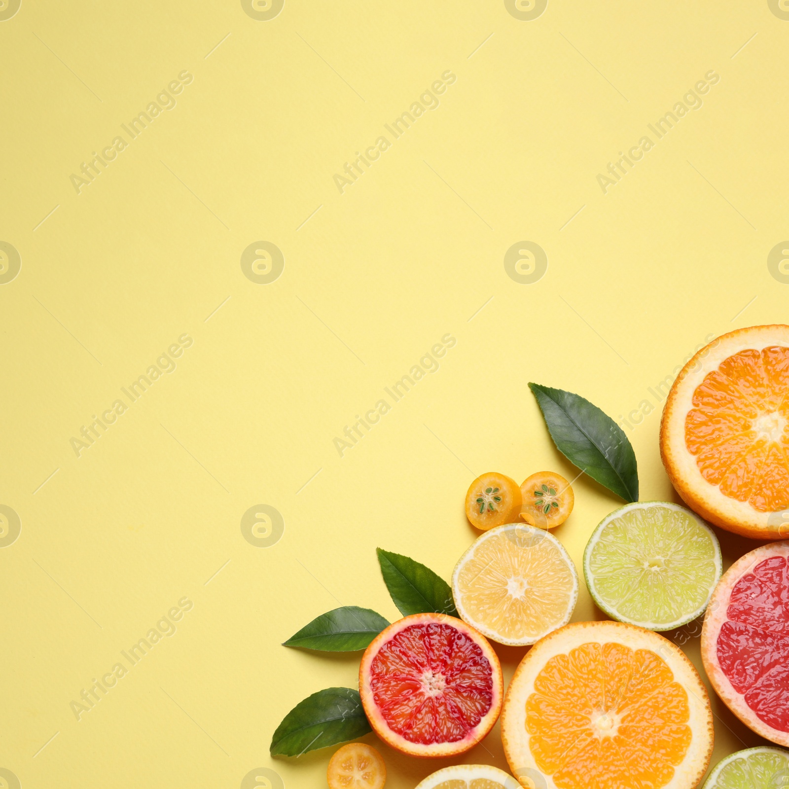 Photo of Fresh juicy citrus fruits with green leaves on light yellow background, flat lay. Space for text