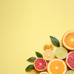 Photo of Fresh juicy citrus fruits with green leaves on light yellow background, flat lay. Space for text