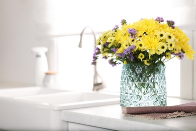 Vase with beautiful chrysanthemum flowers on countertop in kitchen, space for text. Interior design