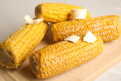 Photo of Delicious boiled corn with butter on wooden board, closeup