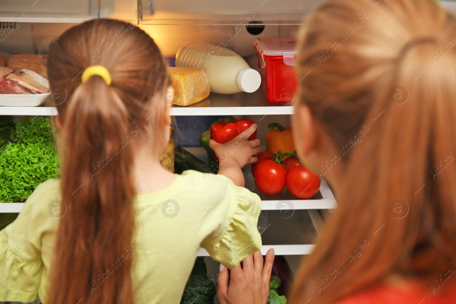 Photo of Young mother and daughter choosing food in refrigerator at home