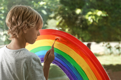 Little boy drawing rainbow on window. Stay at home concept