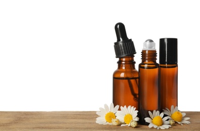 Photo of Chamomile flowers and cosmetic bottles of essential oil on wooden table against white background. Space for text