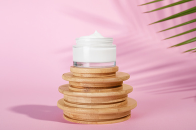 Photo of Open jar of cream on wooden display against pink background