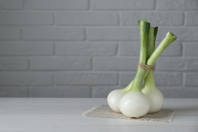 Bunch of fresh green spring onions on white wooden table against brick wall, space for text