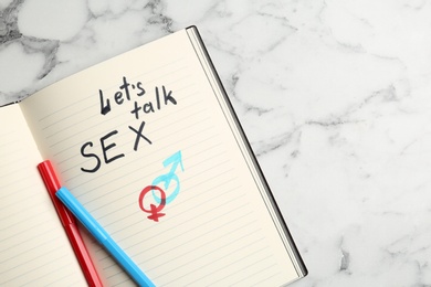 Photo of Notebook with phrase "LET'S TALK SEX" and gender symbols on marble background, top view