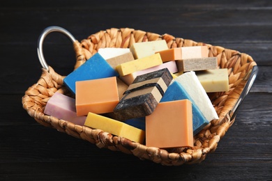 Photo of Many different handmade soap bars in wicker basket on table