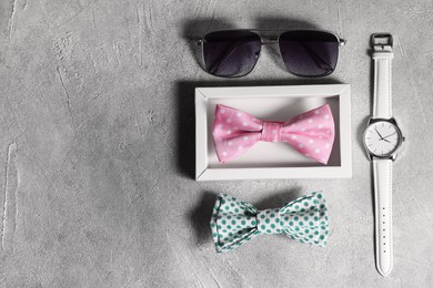 Stylish color bow ties, wristwatch and sunglasses on gray textured background, flat lay. Space for text