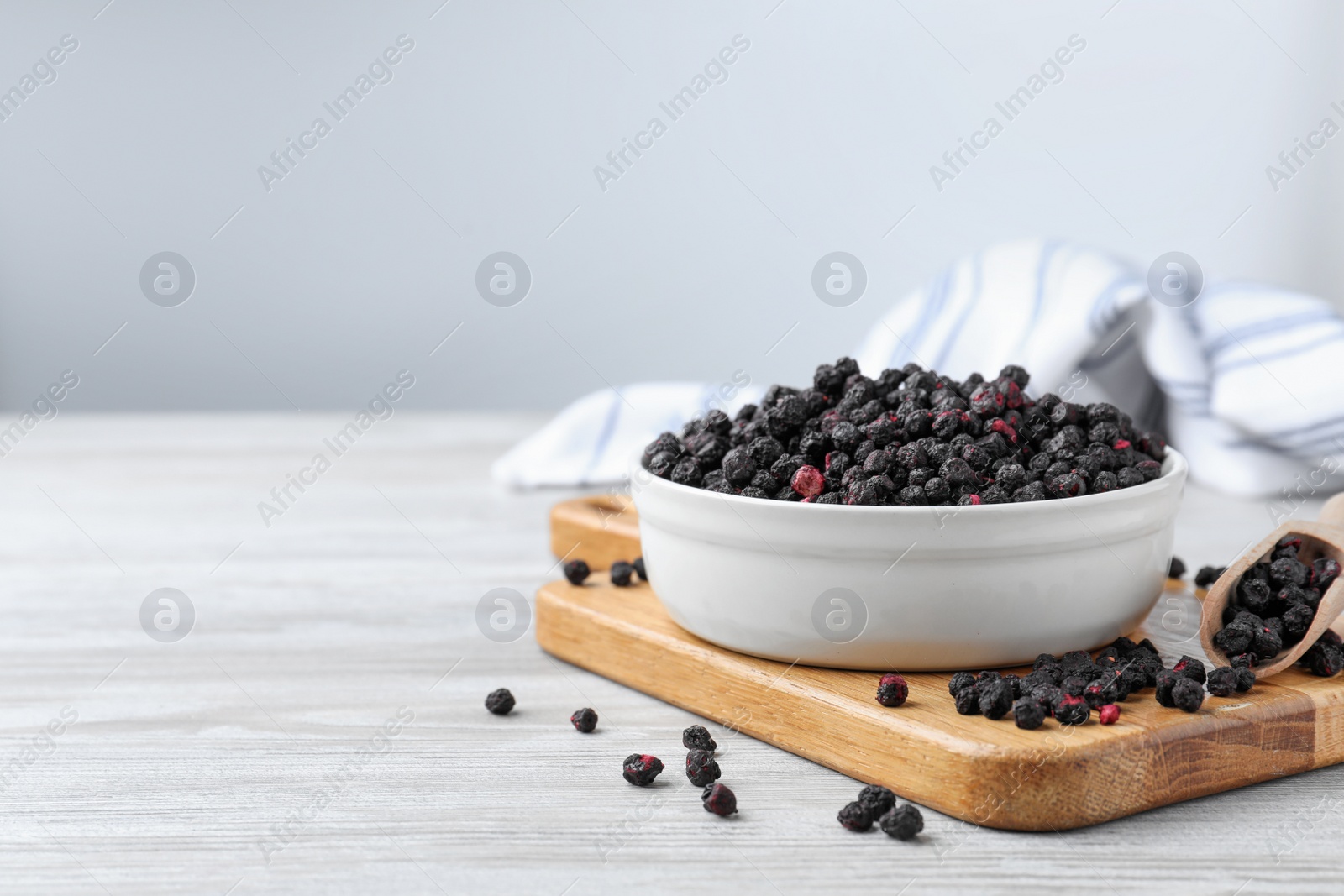 Photo of Bowl and scoop with dried blueberries on white wooden table. Space for text