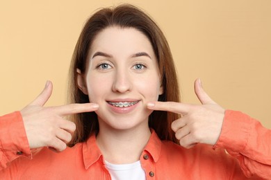 Photo of Portrait of smiling woman pointing at her dental braces on beige background