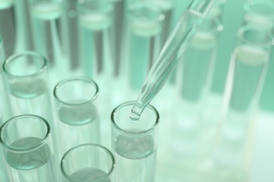 Dripping liquid from pipette into test tube on light green background, closeup