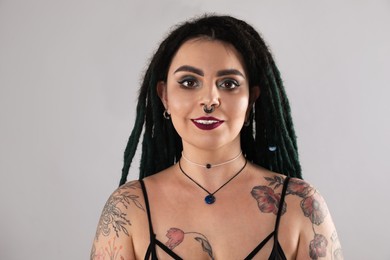 Photo of Beautiful young woman with tattoos on body, nose piercing and dreadlocks against grey background
