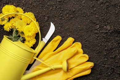 Gardening tools, gloves and flowers on fresh soil, flat lay. Space for text