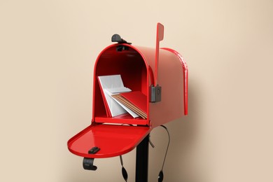 Open red letter box with envelopes against beige background