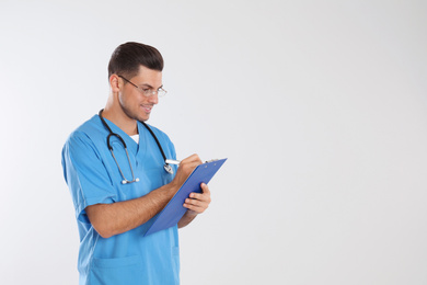 Doctor with stethoscope and clipboard on light grey background. Space for text