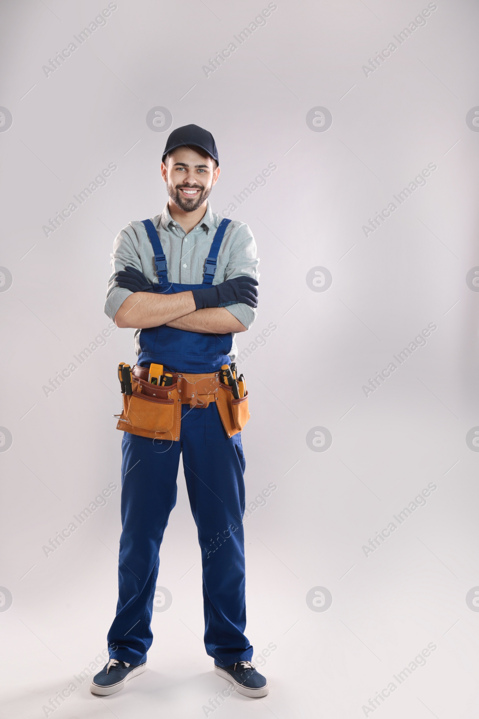 Photo of Full length portrait of construction worker with tool belt on light background