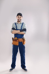 Full length portrait of construction worker with tool belt on light background